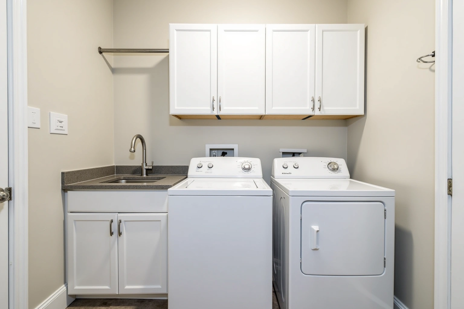 Laundry room with white upper cabinets over a washer and dryer, a hanging rod and a utility sink base cabinet.